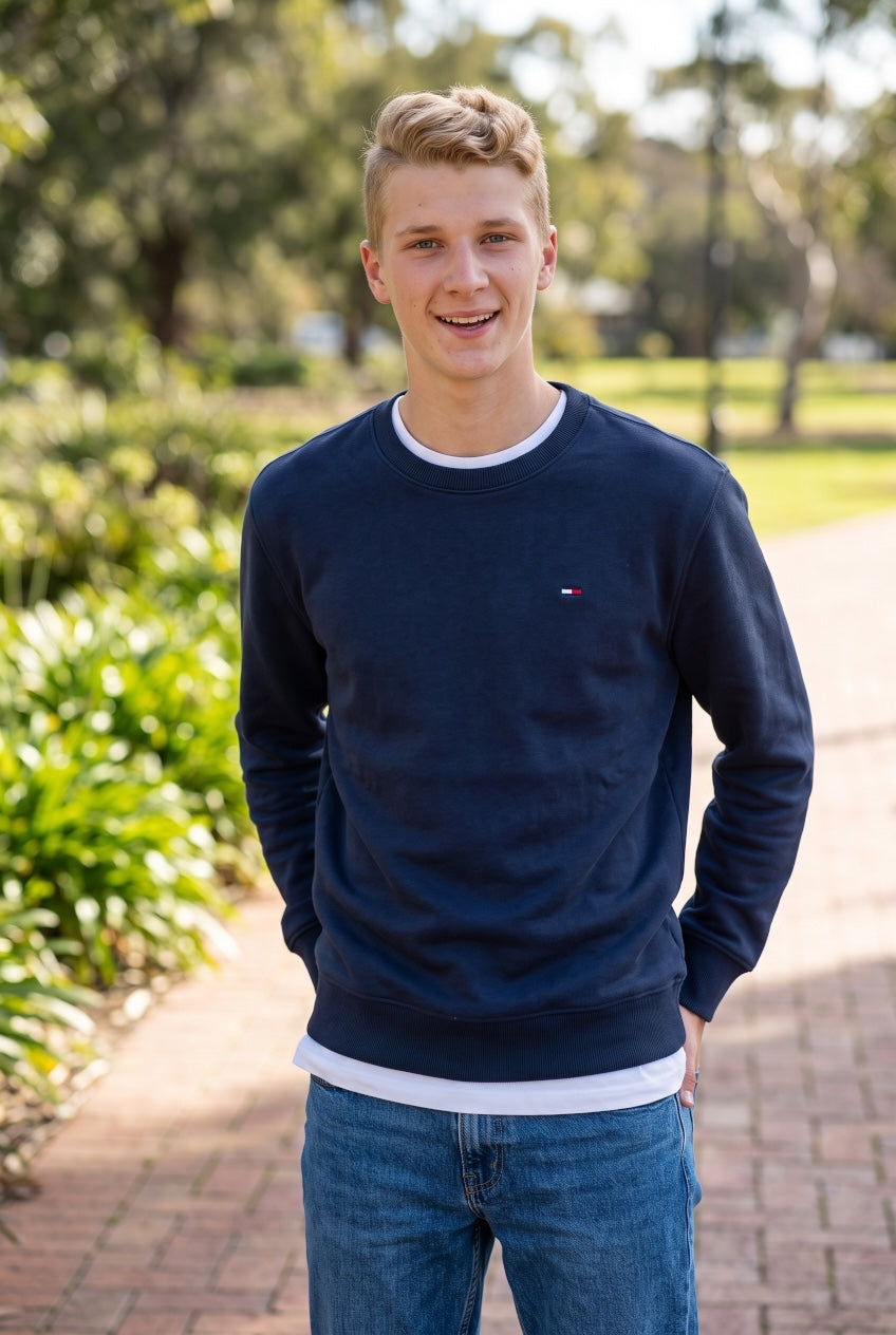 Men's dark blue crew neck sweatshirt with small chest flag logo, worn with jeans