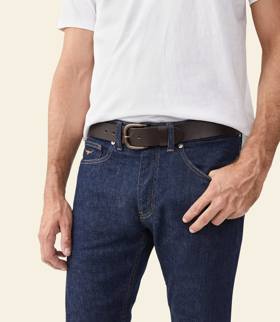 Brown leather belt with metal buckle, worn with blue jeans.