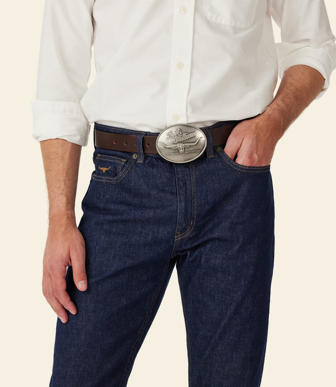 Silver circular RM Williams logo belt buckle on dark denim waistband